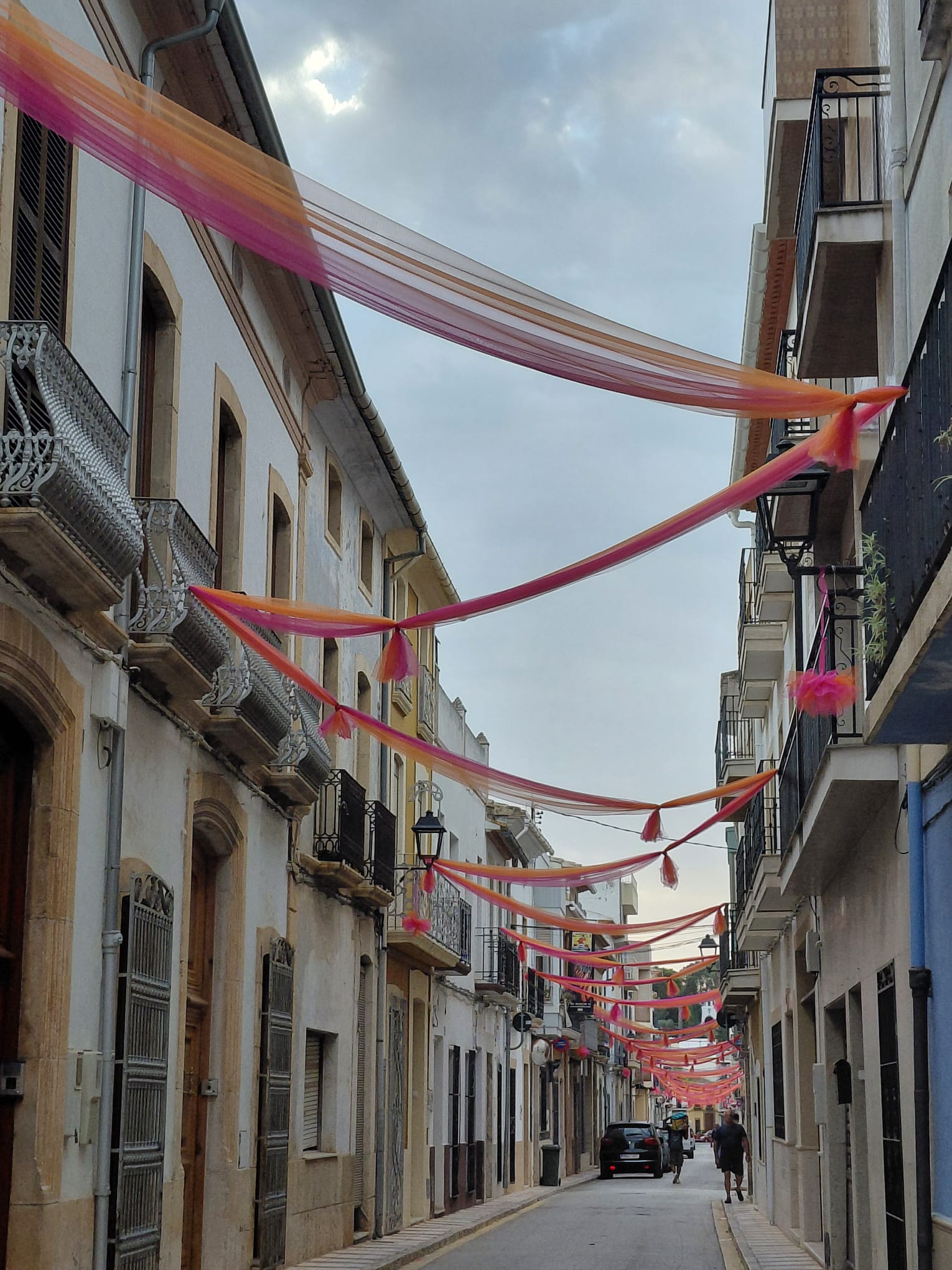 A LES PORTES DE LA FESTA, ADORNANT CARRER. ENTRE TELES I POMPONS, EL CARRER SIGNES MIRA A L'ERMITA