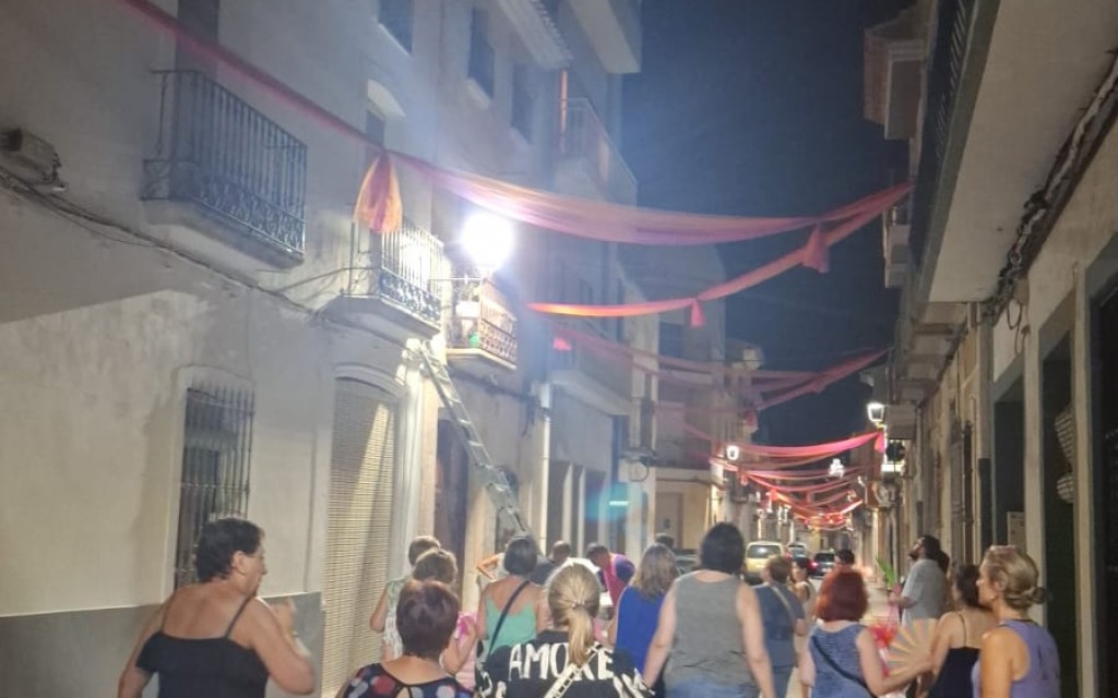 A LES PORTES DE LA FESTA, ADORNANT CARRER. ENTRE TELES I POMPONS, EL CARRER SIGNES MIRA A L'ERMITA